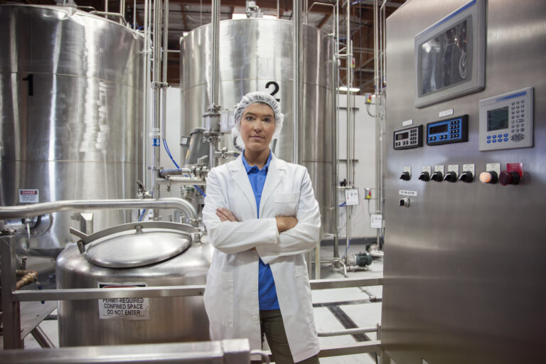 A portrait of a Caucasian female technician near the processing tanks of a bottled water facility.