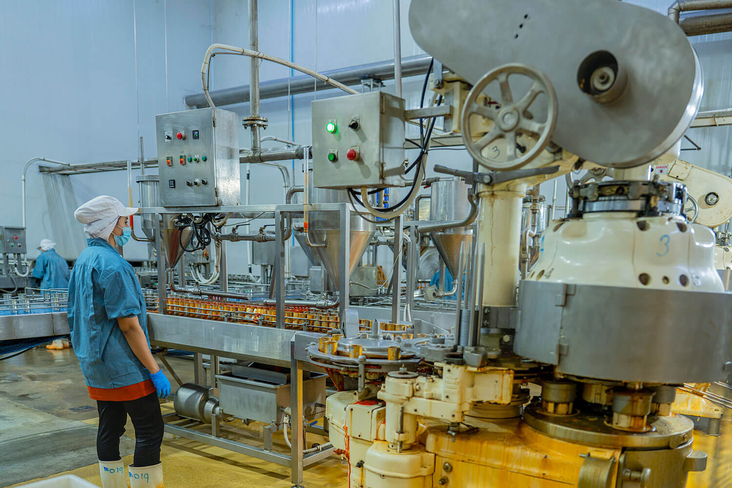 Factory worker in hygienic gear inspecting cans